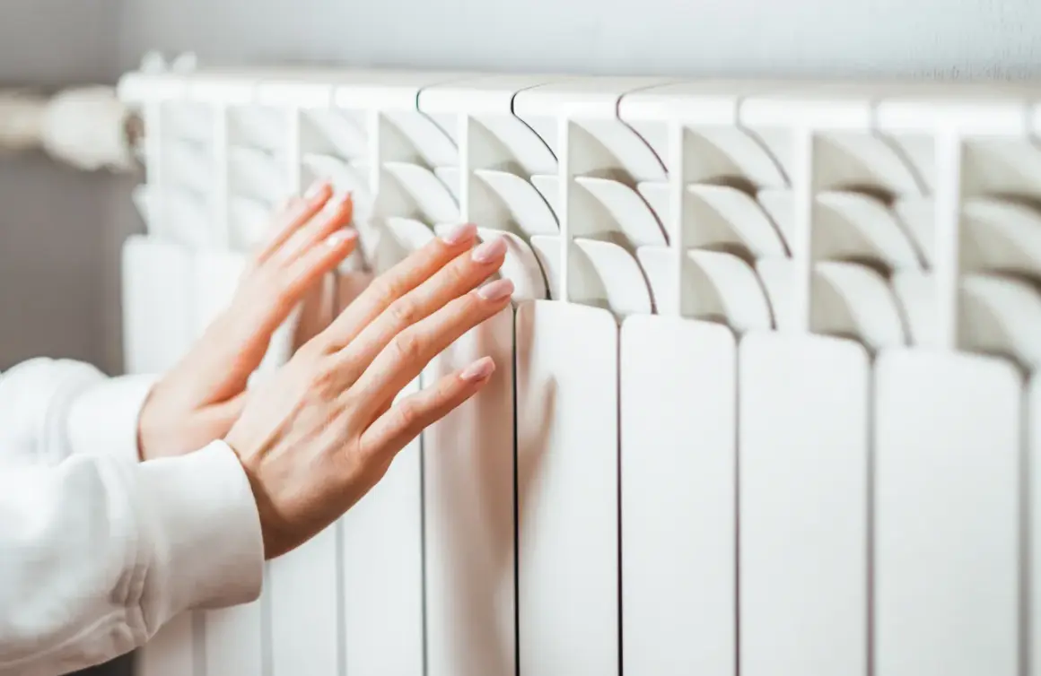 Manos tocando un radiador blanco. Aprende cómo limpiar radiadores para un hogar cálido y eficiente.