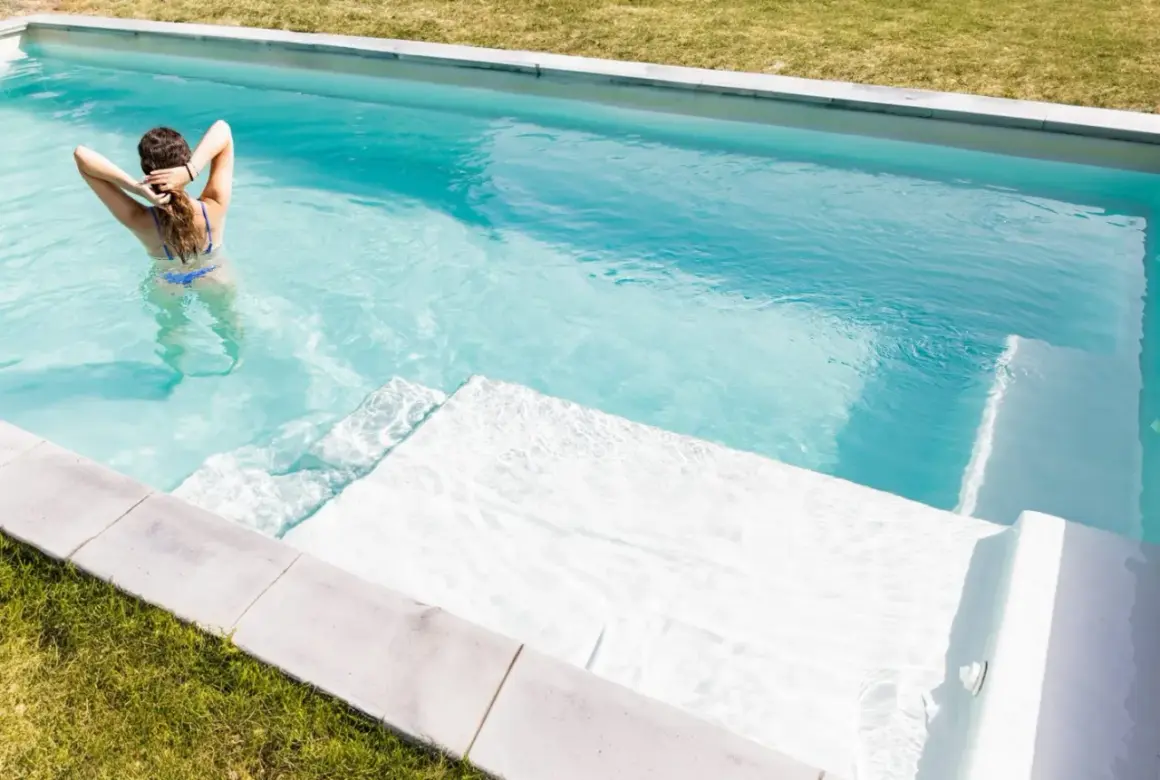 Mujer en bikini azul disfruta de su piscina cristalina, demostrando la facilidad de limpiar piscina sin vaciar agua.