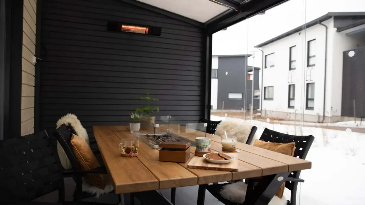 Mesa de madera en terraza cerrada con calefactor, ideal para disfrutar del exterior incluso con nieve.