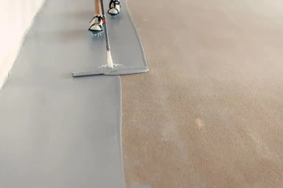 Persona pintando el suelo con una llana, aplicando una capa gris sobre una superficie texturizada.