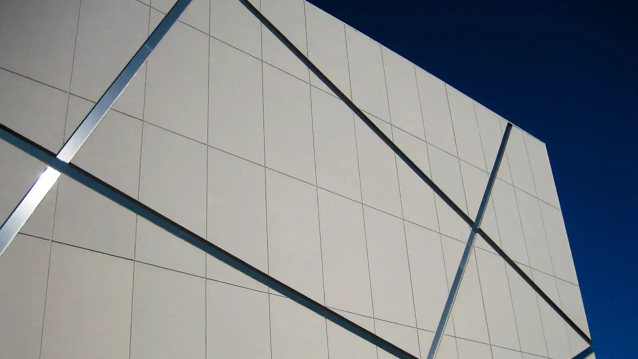Fachada moderna con paneles de pladur para exterior, unidos por perfiles metálicos, contra un cielo azul intenso.