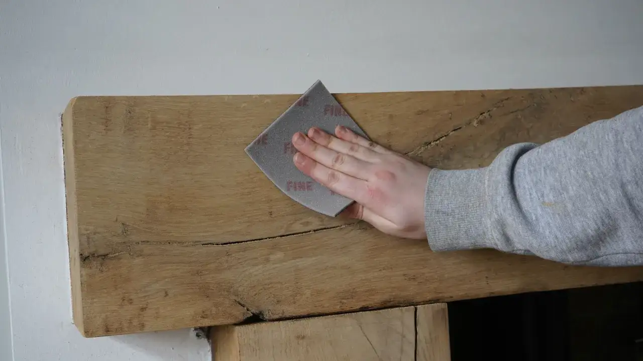 Mano lijando madera rústica, preparándola para como pintar madera ya pintada.