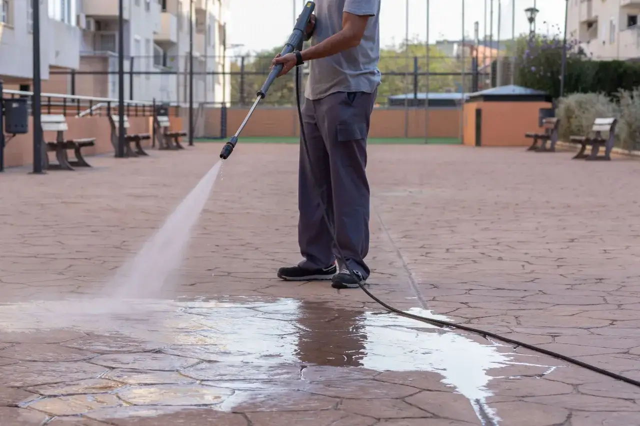 Persona limpiando el suelo de una terraza exterior con una hidrolimpiadora. El agua a presi&oacute;n deja el suelo brillante y limpio.
