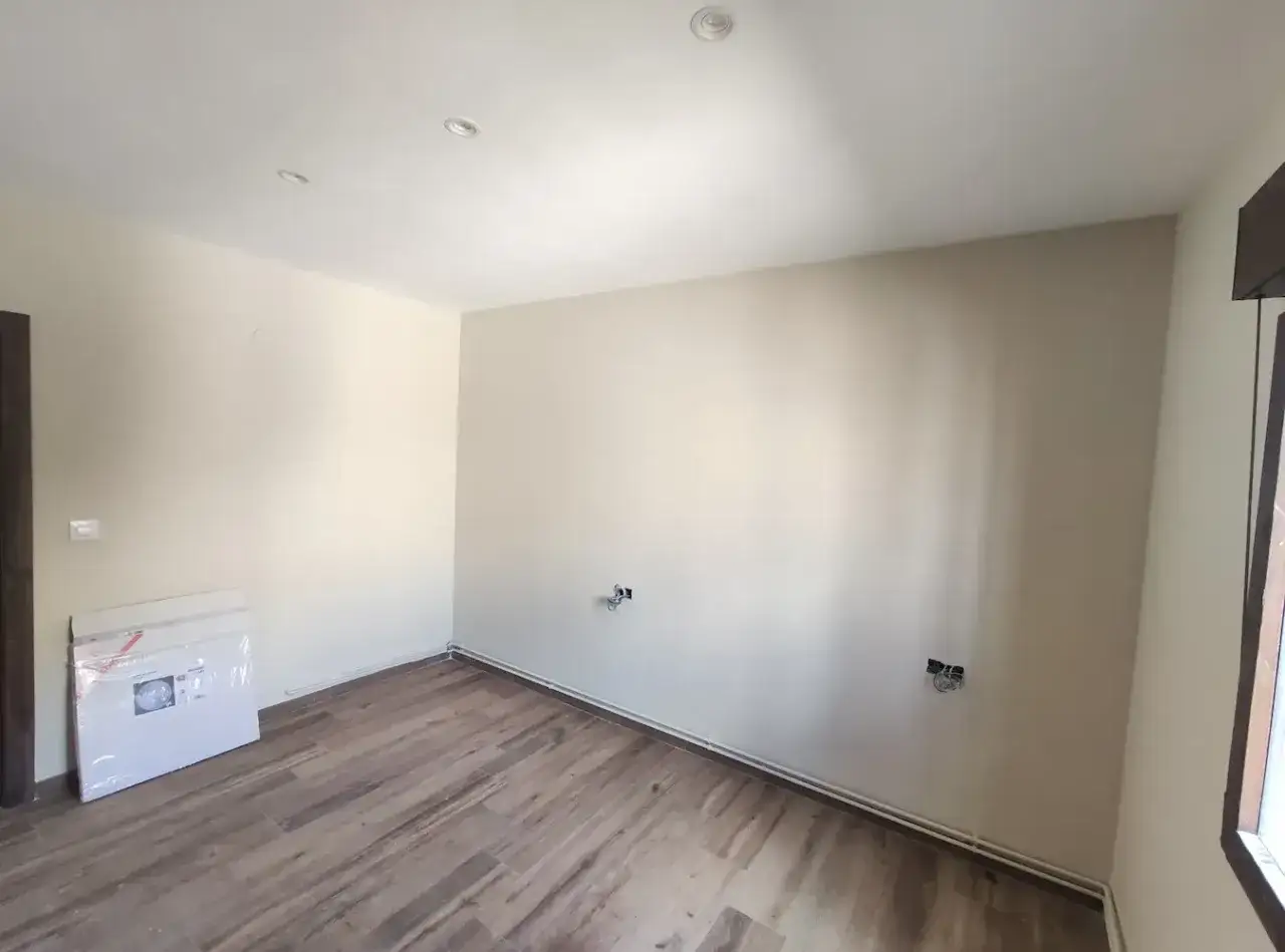 Habitación vacía con paredes claras y suelo de madera. Se ve un paquete en el suelo. Ideal para calcular el precio pintar piso.