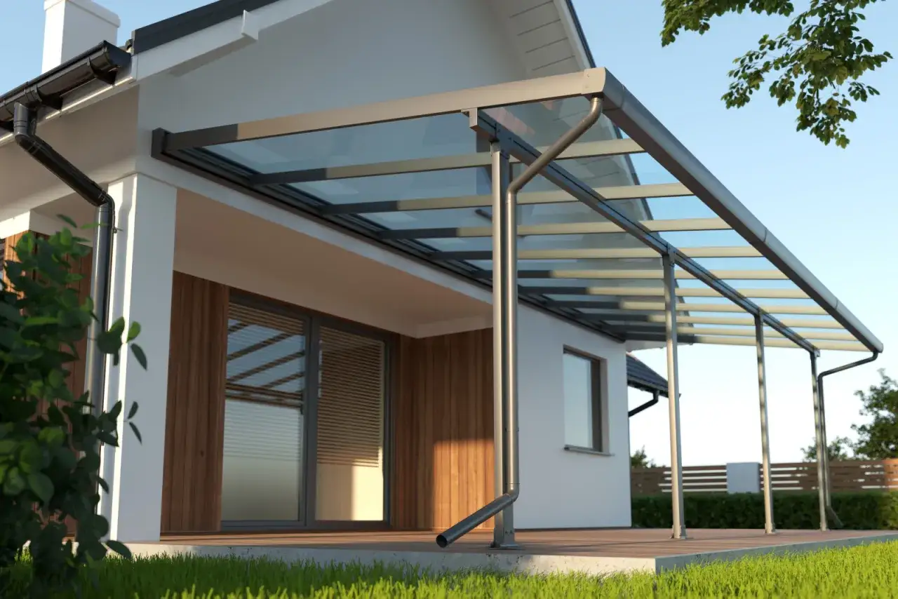 Modernos tipos de toldos con estructura met&aacute;lica y cubierta de cristal protegen una terraza de madera junto a una casa.