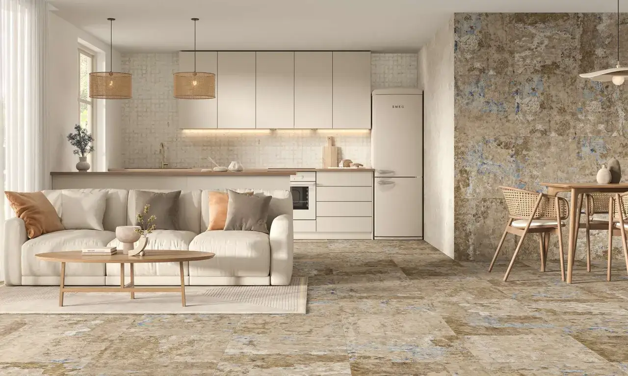 Salón y cocina modernos con suelo de cemento pulido de aspecto rústico, sofá beige, muebles de cocina claros y pared decorativa.