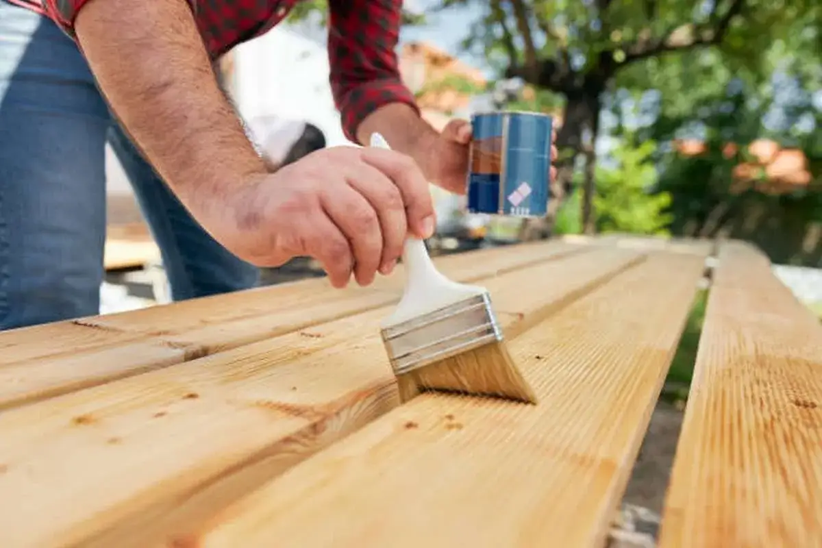 Hombre aplicando protector a madera para exterior con brocha. Aprende como tratar la madera para exterior y protegerla.