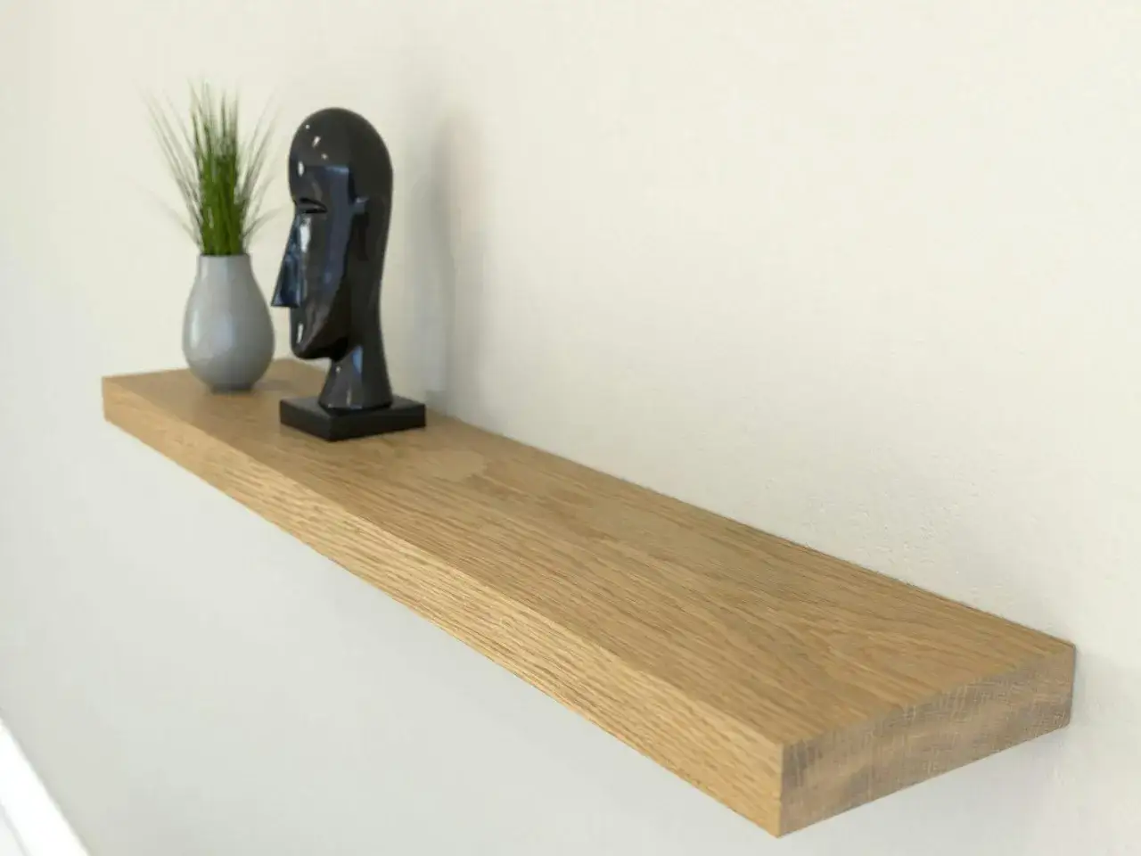 Estantería flotante de madera, ideal para poner baldas en pared sin escuadras. Decorada con un busto negro y una planta.