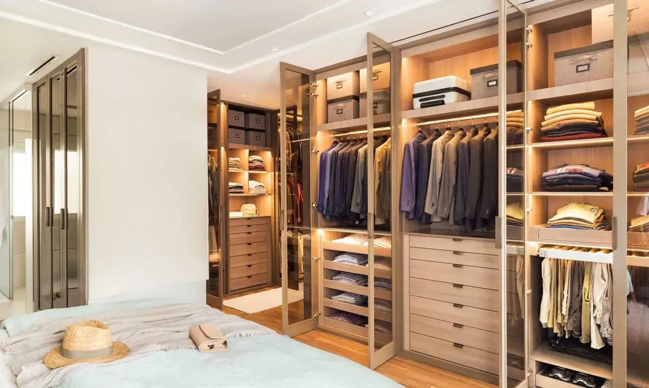 Un vestidor moderno con puertas de cristal, trajes colgados, cajones y estantes organizados. Ideas para como hacer un vestidor funcional y elegante.