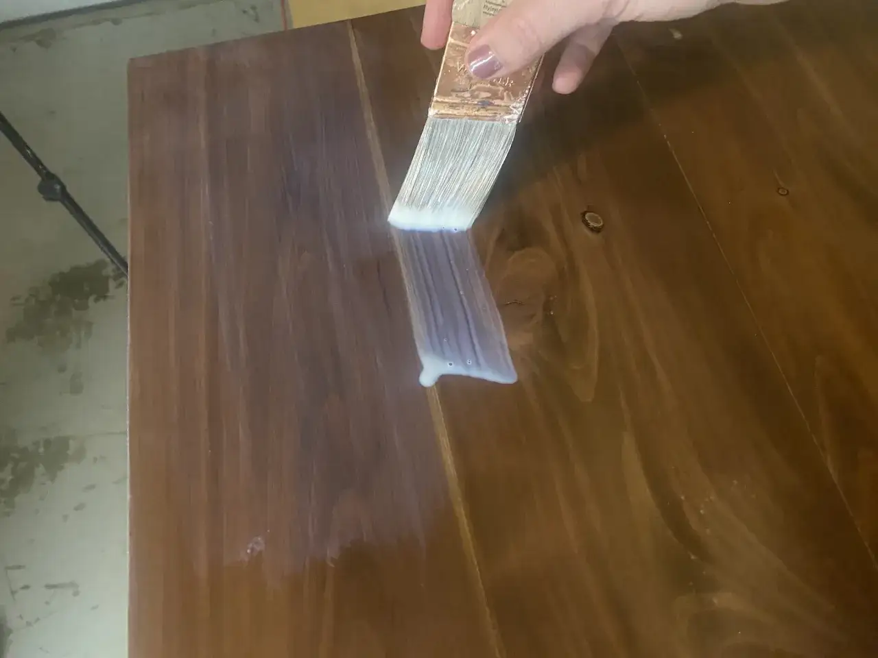 Mano aplicando barniz con brocha para pintar mesa de madera.