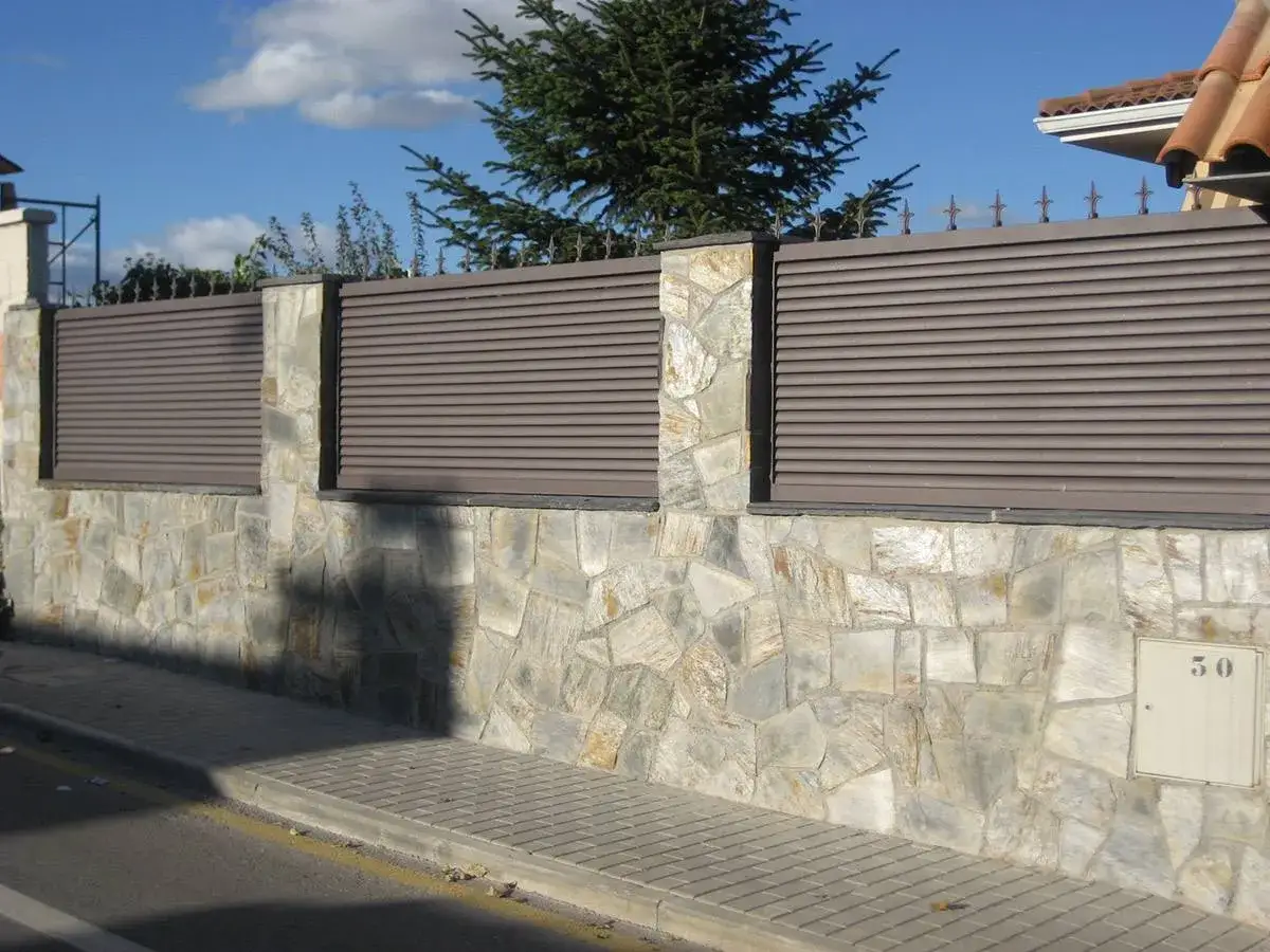 Muro de piedra con lamas horizontales, un ejemplo de tipos de vallas para chalet que combinan est&eacute;tica y privacidad.