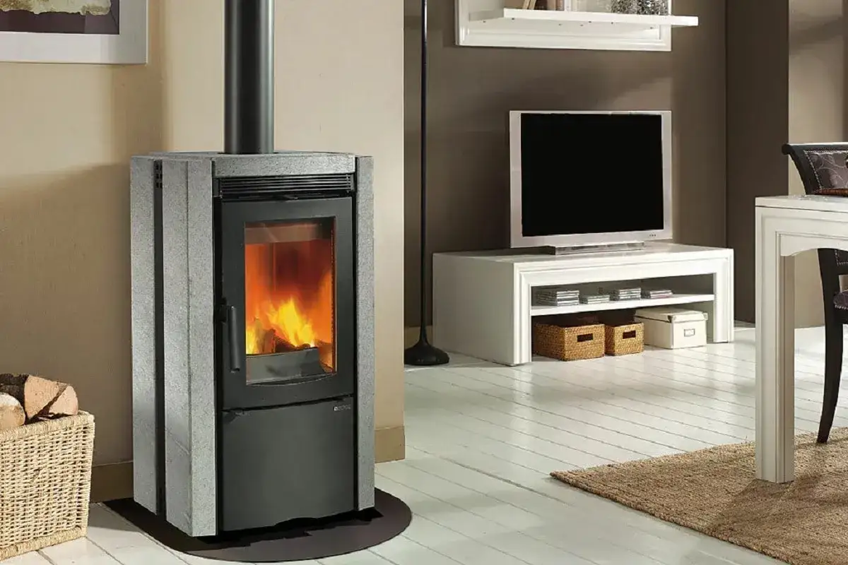 Estufa de leña moderna, uno de los tipos de estufas que calientan el hogar. Chimenea, leña y TV en salón.