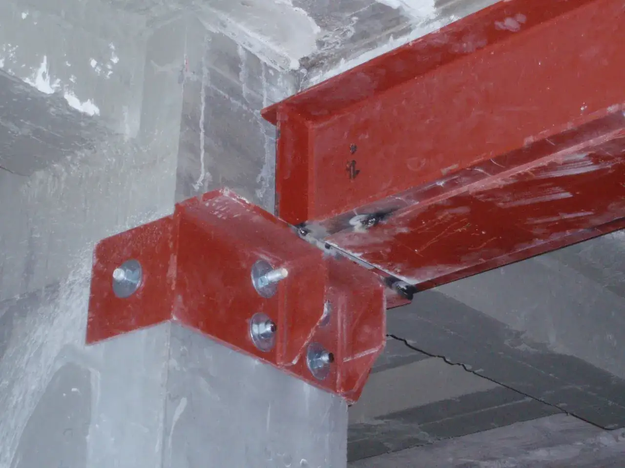 Detalle de una viga met&aacute;lica roja unida a un pilar de hormig&oacute;n con pernos. Se puede taladrar una viga de hormig&oacute;n para fijar estructuras.
