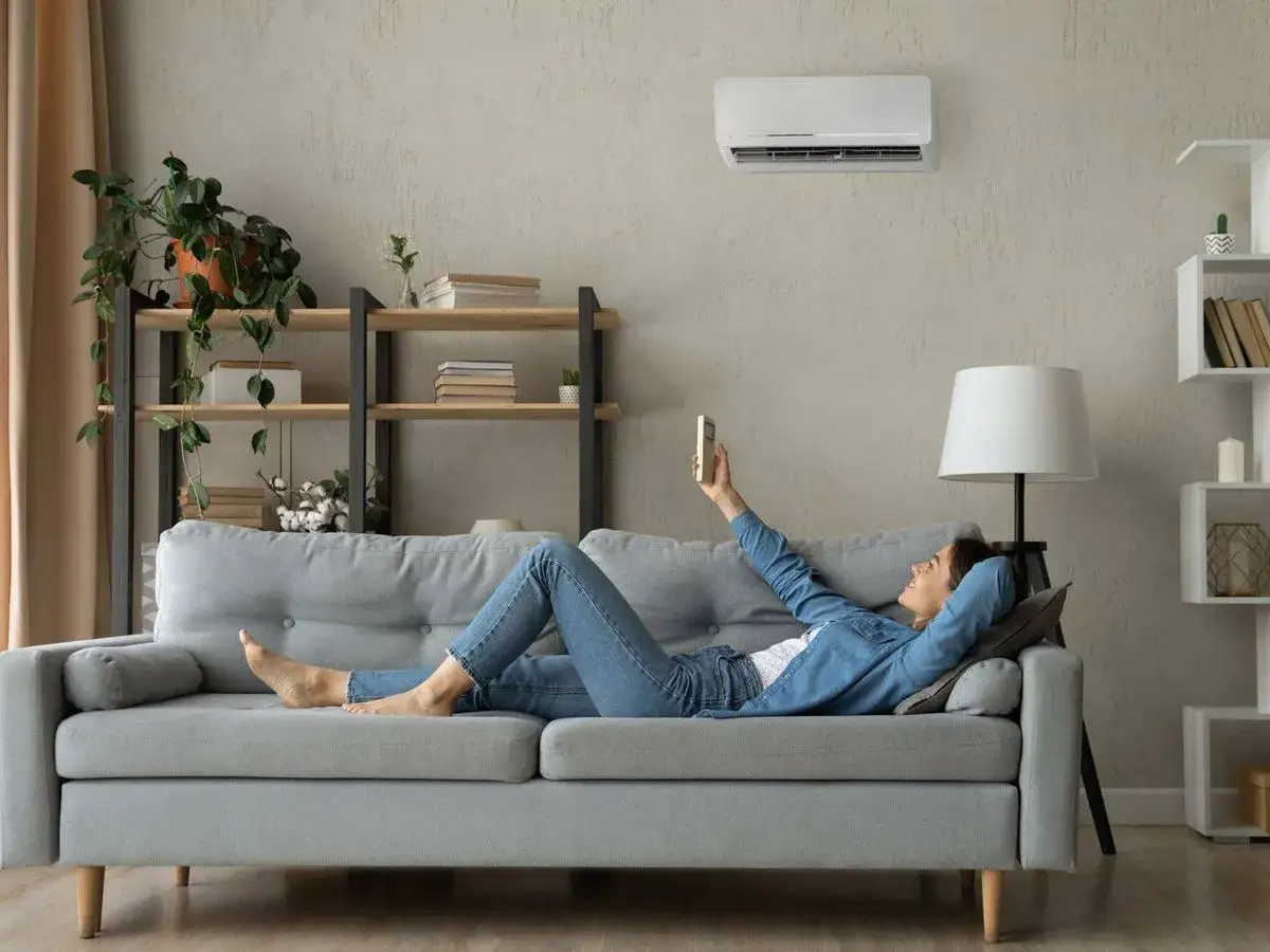 Mujer relajada en sof&aacute;, disfrutando de la temperatura ideal aire acondicionado.