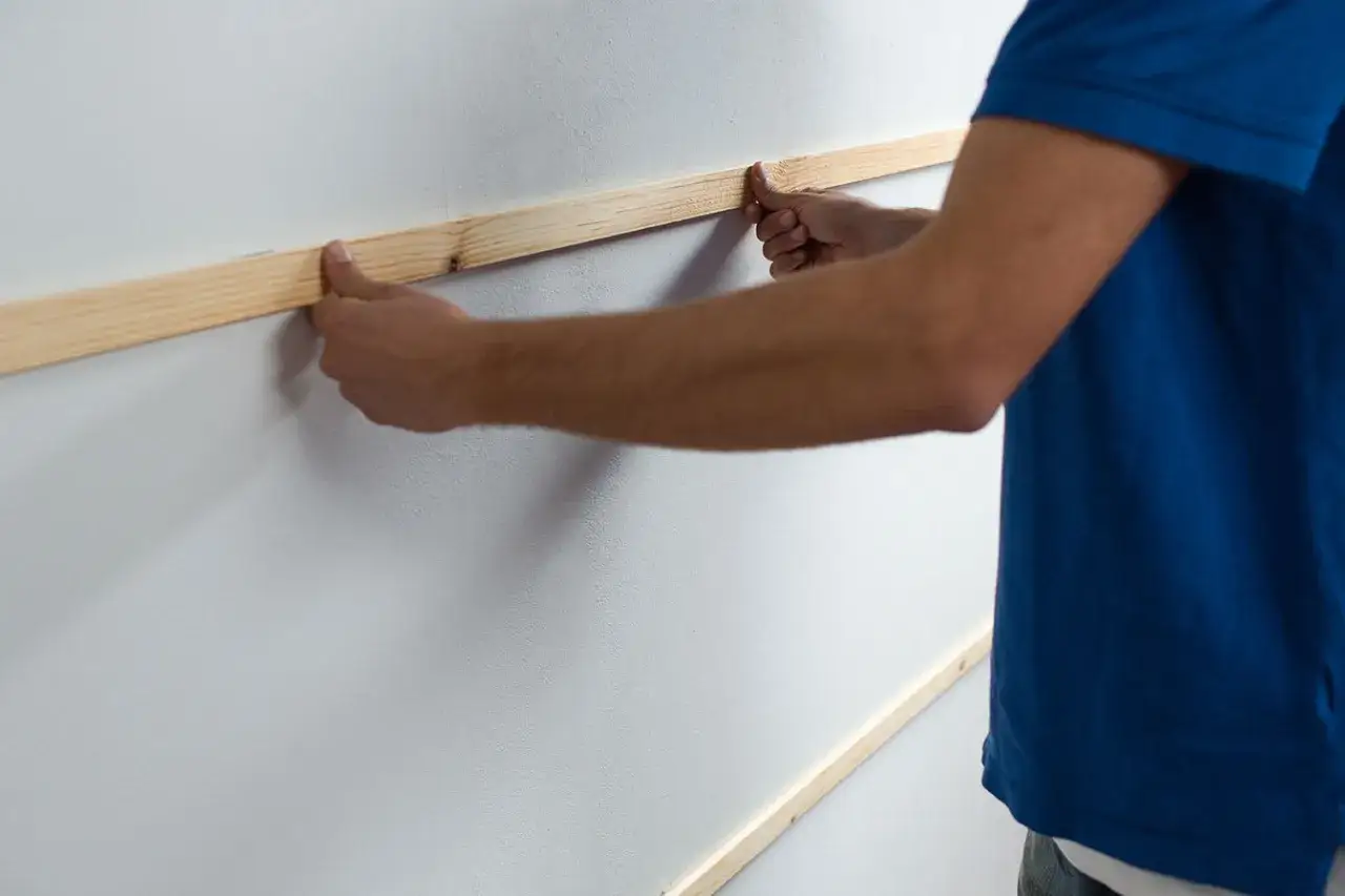 Man placing wooden slats on a white wall, demonstrating como poner listones de madera en la pared.