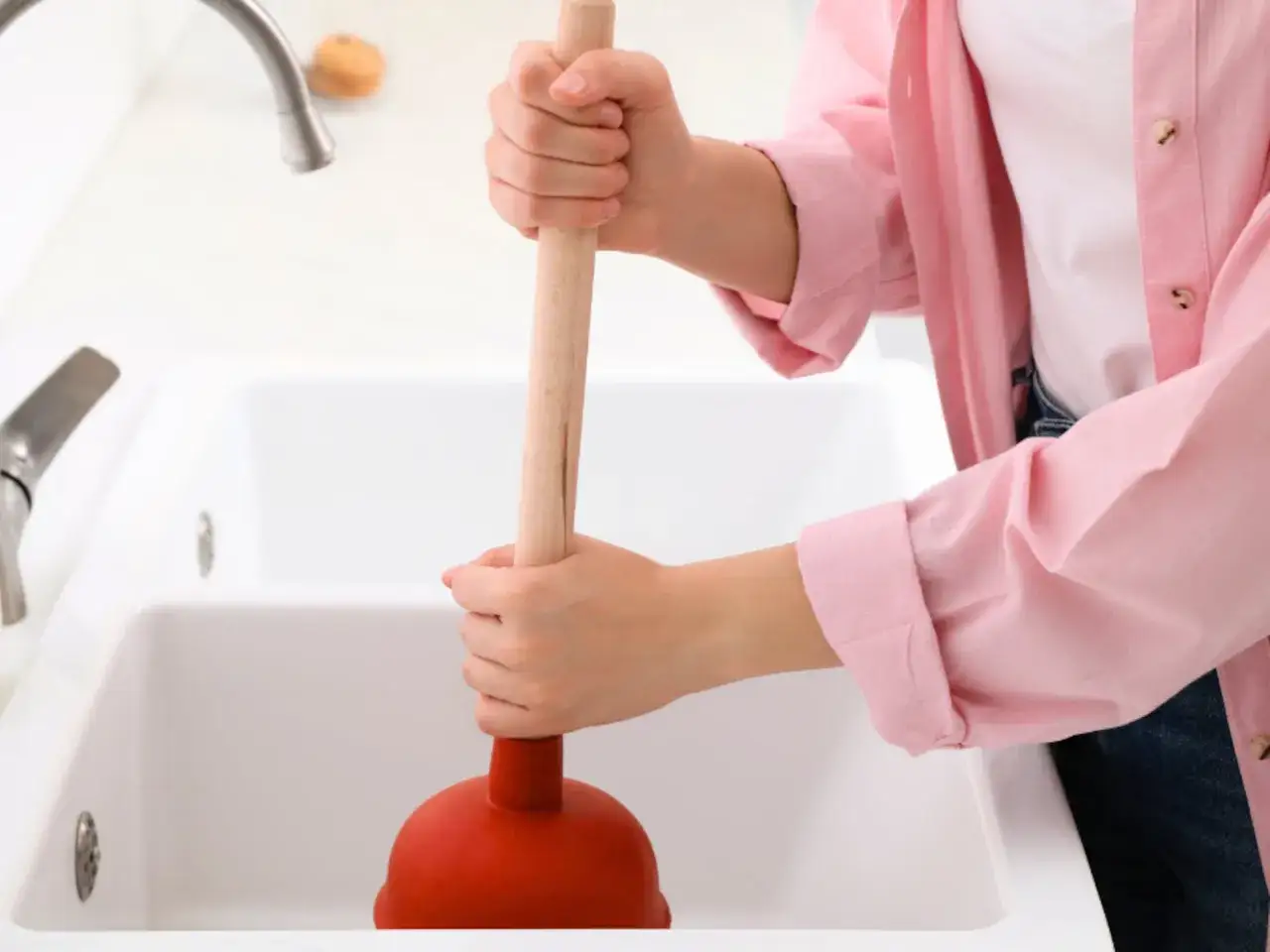 Mano sujetando un desatascador casero para arreglar un desagüe.