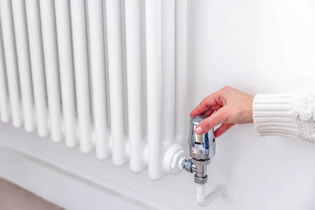 Mano ajustando el termostato de un radiador blanco. ¿Por qué suenan los radiadores? Quizás el aire atrapado o la presión.