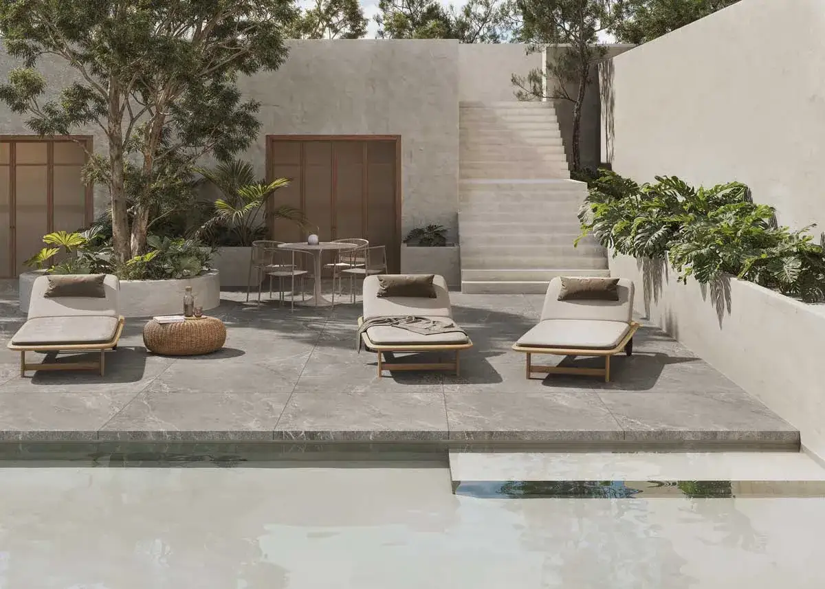 Terraza moderna con tumbonas y piscina. El suelo de baldosas grises, con una norma resbaladicidad C1, C2, C3, ofrece seguridad y estilo.