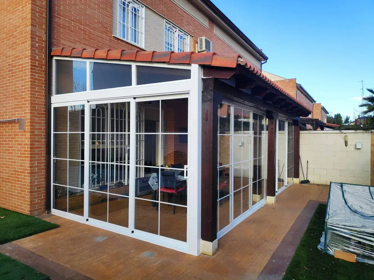 Modernos tipos de cerramientos de cristal con marcos blancos, integrados en una casa de ladrillo con un porche de madera.