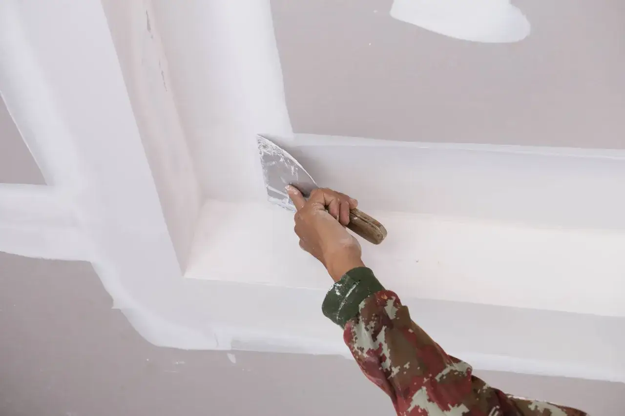 Mano con esp&aacute;tula aplica masilla para reparar techo escayola.