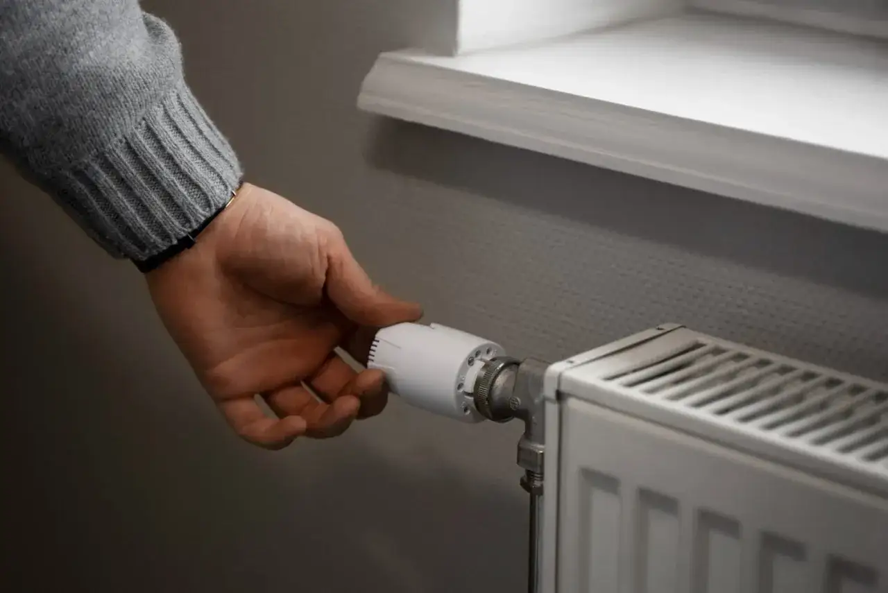 Mano ajustando el termostato de un radiador que gotea.