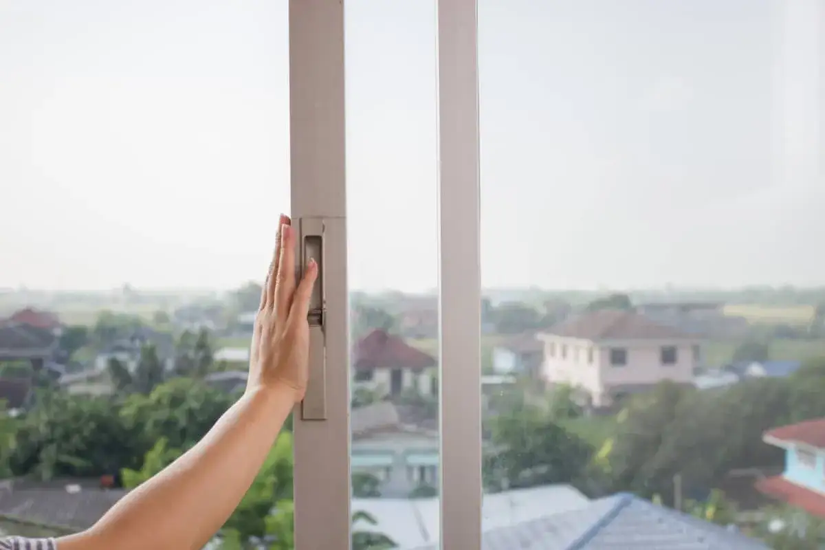 Mano sujetando el marco de una ventana corredera, útil para saber como aislar ventanas correderas y mejorar la eficiencia energética.