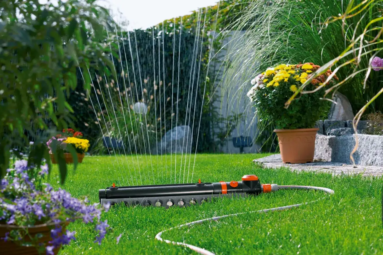 Instalación de riego automático en césped verde, con aspersores rociando agua sobre flores y plantas.