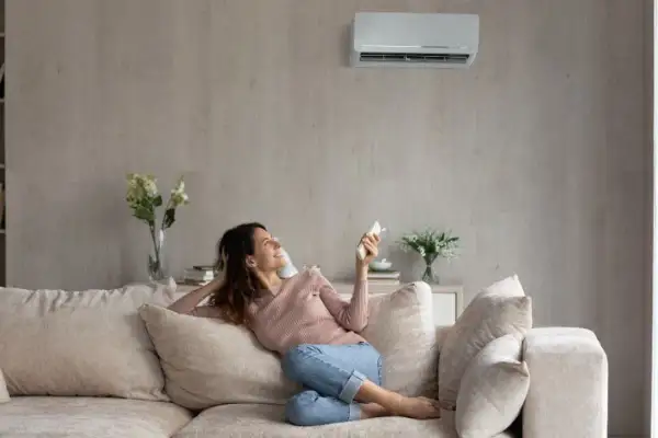Mujer sonríe en el sofá, disfrutando de la temperatura ideal del aire acondicionado.