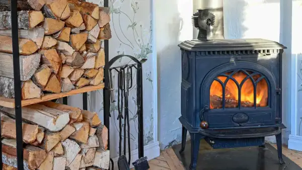 Estufa de leña con fuego encendido y leña apilada. Un ventilador para estufa de leña opiniones positivas sobre su eficiencia.