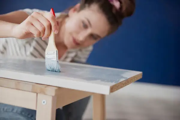 Mujer pintando muebles de melamina con brocha y pintura azul claro.
