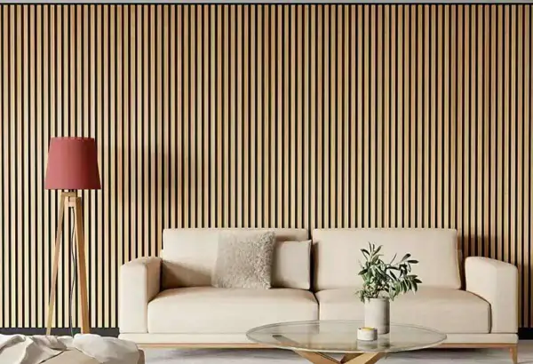 Una pared con listones de madera verticales, ideal para quienes buscan ideas sobre como poner listones de madera en la pared. Un sofá beige y una lámpara roja completan la escena.