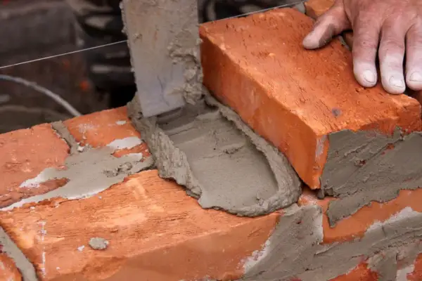 Mano coloca ladrillo sobre mortero fresco. Aprende como hacer mortero para construir.