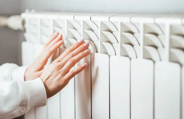 Manos tocando un radiador blanco. Aprende cómo limpiar radiadores para un hogar cálido y eficiente.