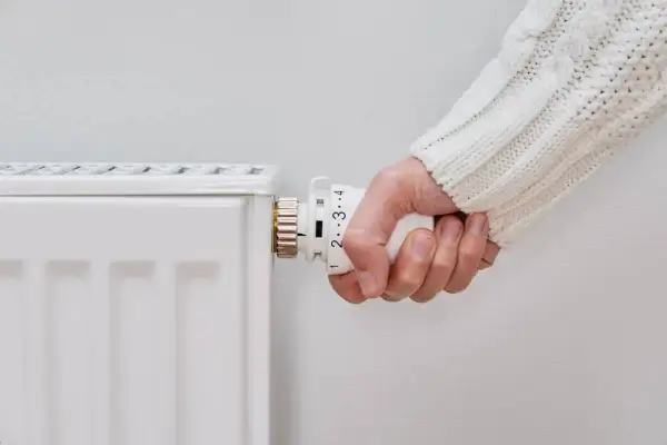 Mano ajustando el termostato de un radiador blanco. Parece que el radiador no calienta, a pesar de los ajustes.