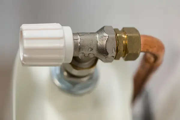 Detalle de una llave de radiador que gotea, con gotas de agua visibles en la conexión metálica.