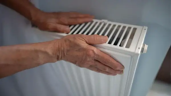 Manos sobre un radiador blanco, sintiendo el calor. ¿Por qué suenan los radiadores?