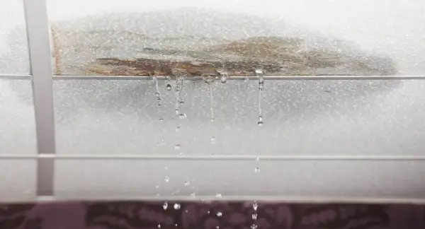 Gotas de agua caen de un techo manchado, señal de que la impermeabilización de tejados es urgente.