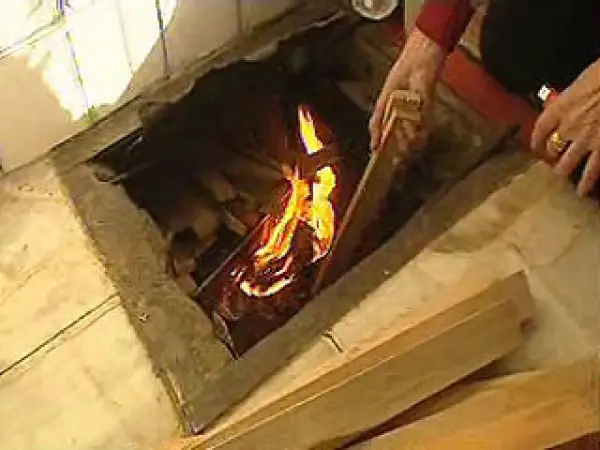 Manos añaden leña a un fuego en un hogar, brindando **gloria calefacción** a la estancia.