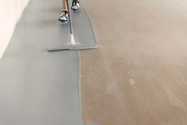 Persona pintando el suelo con una llana, aplicando una capa gris sobre una superficie texturizada.