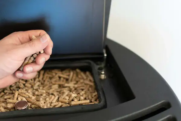 Mano añadiendo pellets a una estufa de leña. Preparando la instalación de estufa pellets para un invierno cálido.